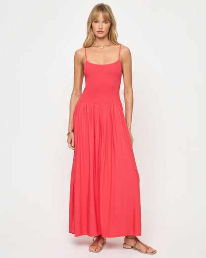 Front view of a model wearing the LSPACE Misha Midi in pout, featuring thin spaghetti straps, a square neckline, a smocked fitted bodice, and a full flowing coral pink skirt.