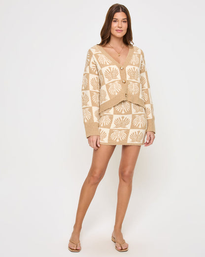 Front view of a model wearing the LSPACE Shell Be There Skirt in seashell jacquard, a fitted knit mini skirt with a checkered seashell print in tan and cream, worn as a coordinating set with the matching cardigan.