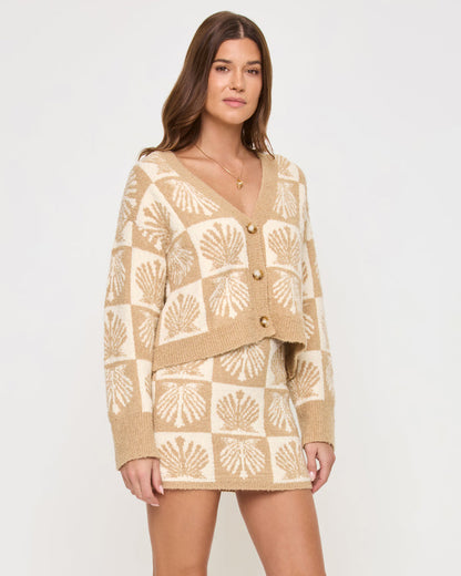 Angled front view of a model wearing the LSPACE Shell Be There Skirt in seashell jacquard, highlighting the knit texture and the checkered seashell pattern in tan and cream, paired with the matching cardigan.