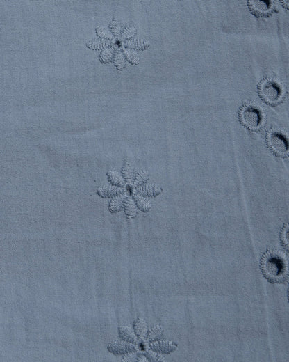 Close-up of a dusty blue fabric with embroidered floral motifs and eyelet embroidery.